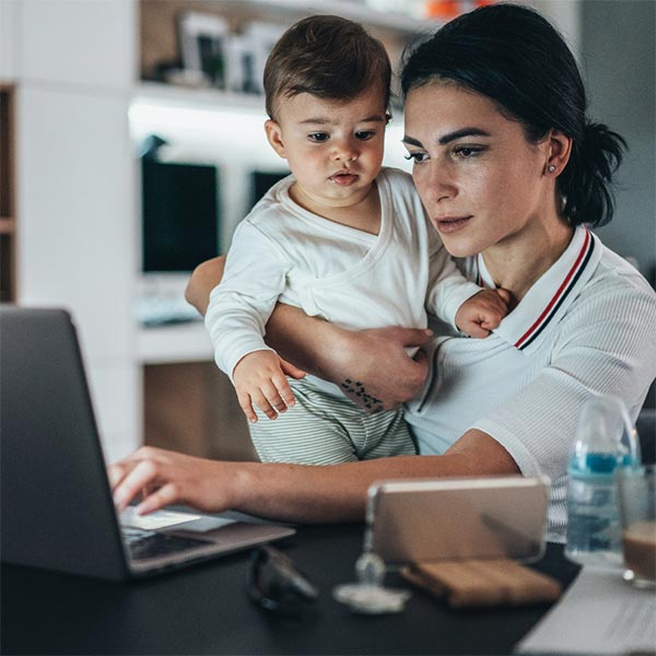 Mother holding toddler while working on her laptop