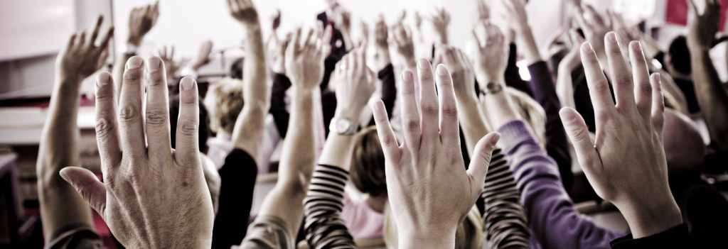 Close up of a room full of people with their hands raised